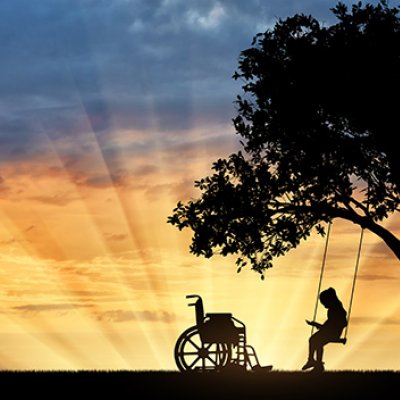 A silhouette image of a child on a swing under a tree with a wheelchair nearby.